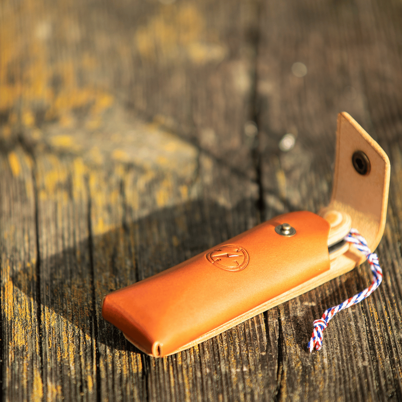 Étui en cuir patiné posé sur du bois brut, l'accessoire indispensable pour les pique-niques chics et le bivouac.