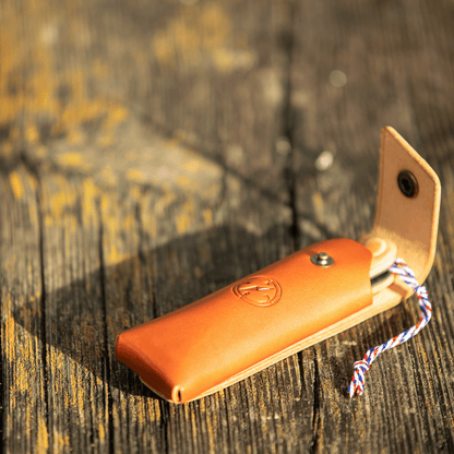 Étui en cuir patiné posé sur du bois brut, l'accessoire indispensable pour les pique-niques chics et le bivouac.