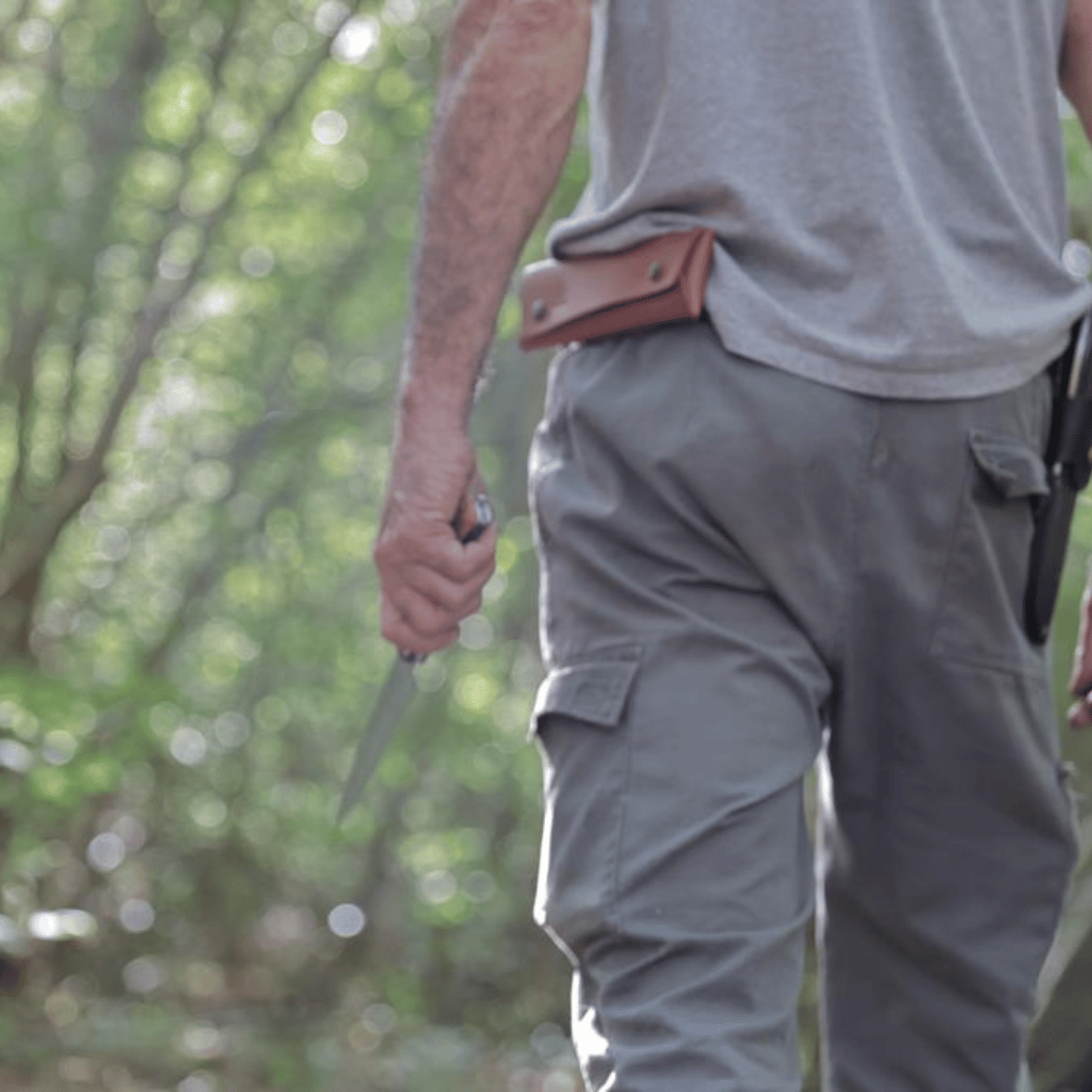 Homme portant l'étui en cuir artisanal à la ceinture lors d'une randonnée en forêt, couteau en main.
