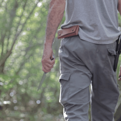 Homme portant l'étui en cuir artisanal à la ceinture lors d'une randonnée en forêt, couteau en main.